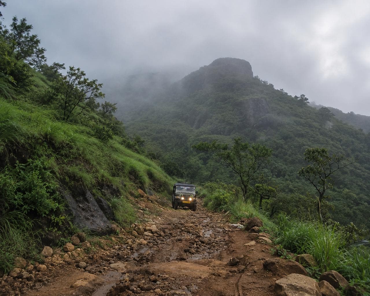 A jeep climbing a washed-out track towards a rock peak in the Ghats