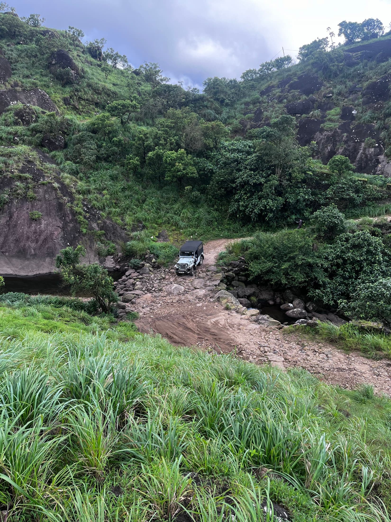 A jeep on the track below the Urumbikkara hilltop, grass and cloud either side