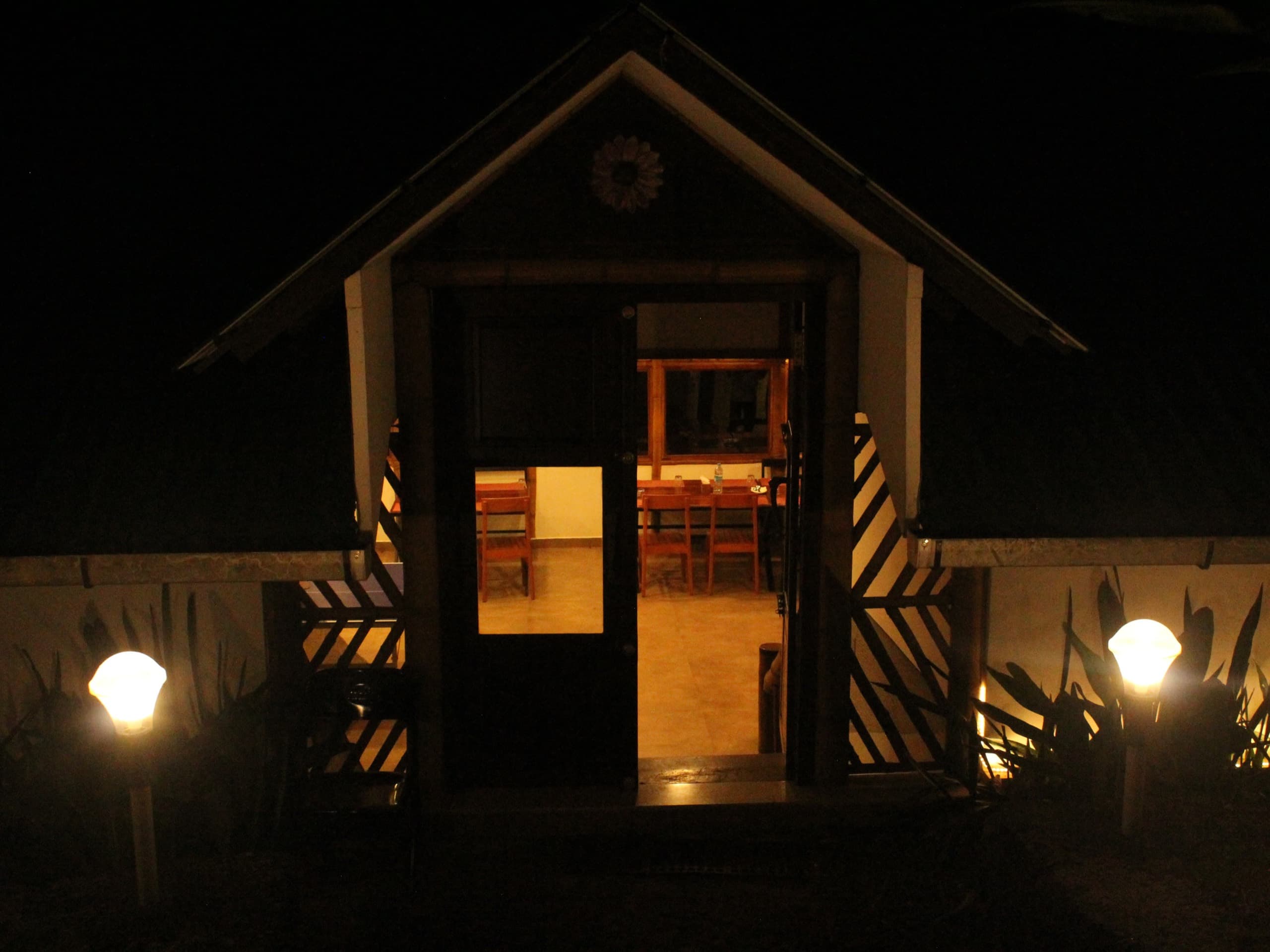 A cottage porch, lamps lit